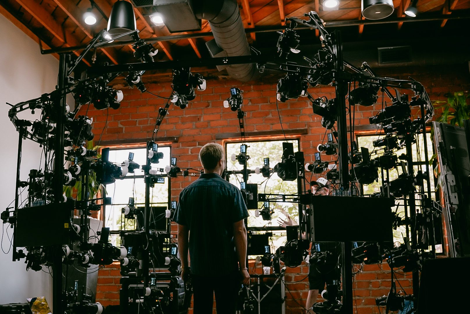 A wall of cameras and monitors fills a brick studio, an attendee standing with his back to the lens.