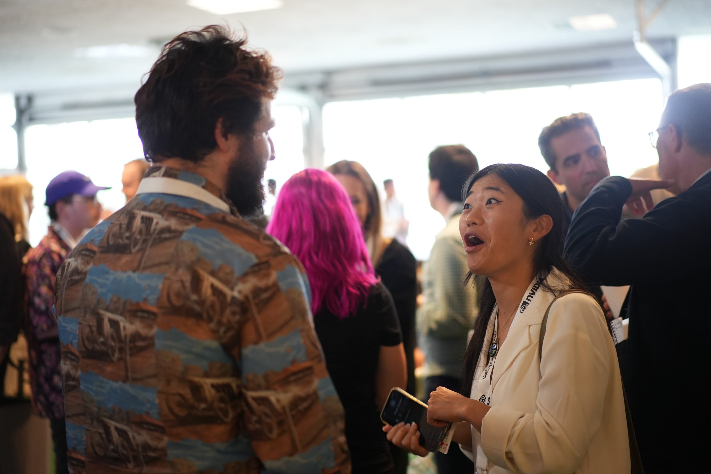 Attendees mid-conversation at a reception, one woman laughing, drinks in hand.