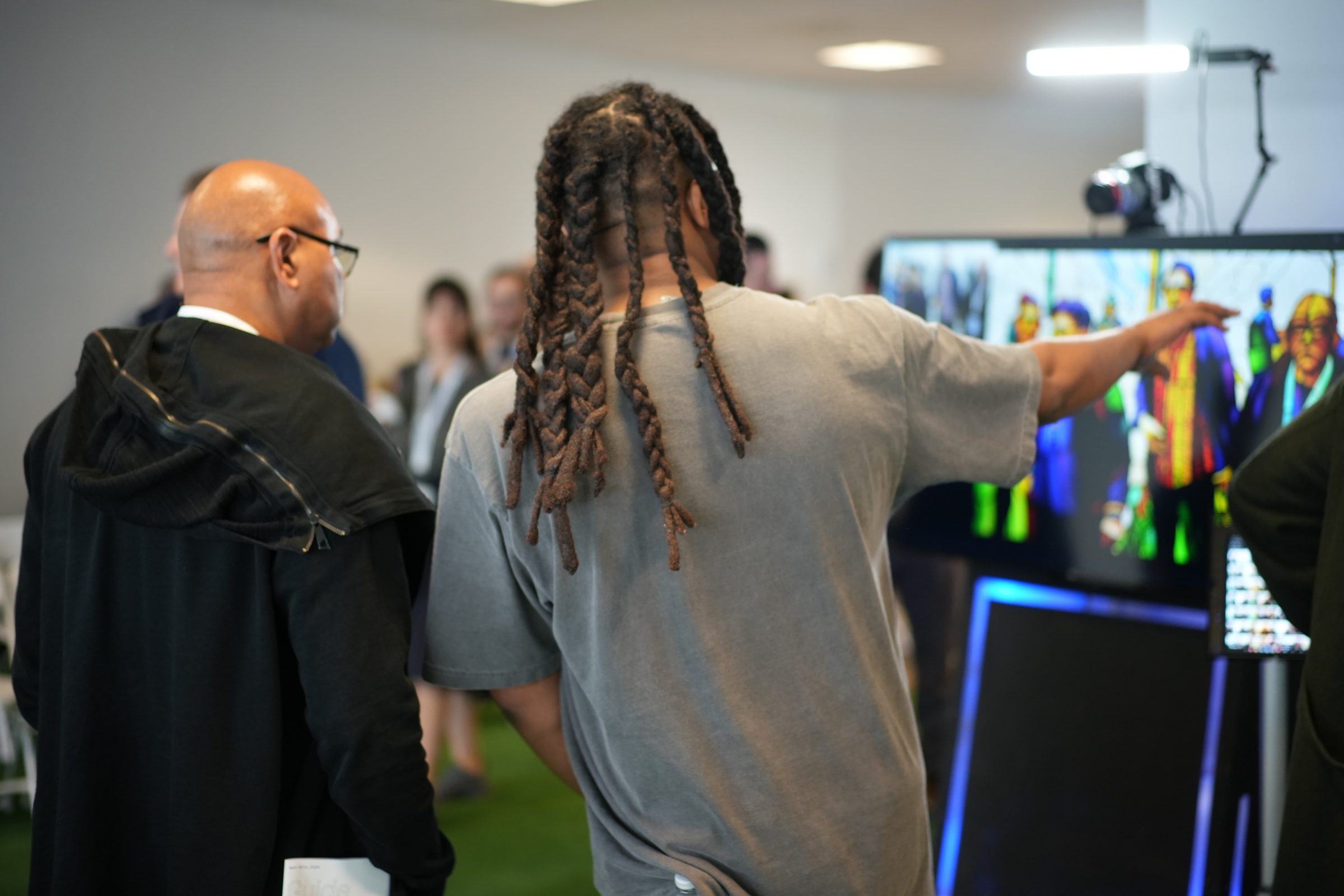 An attendee points at a screen of colorful AI faces while another watches.