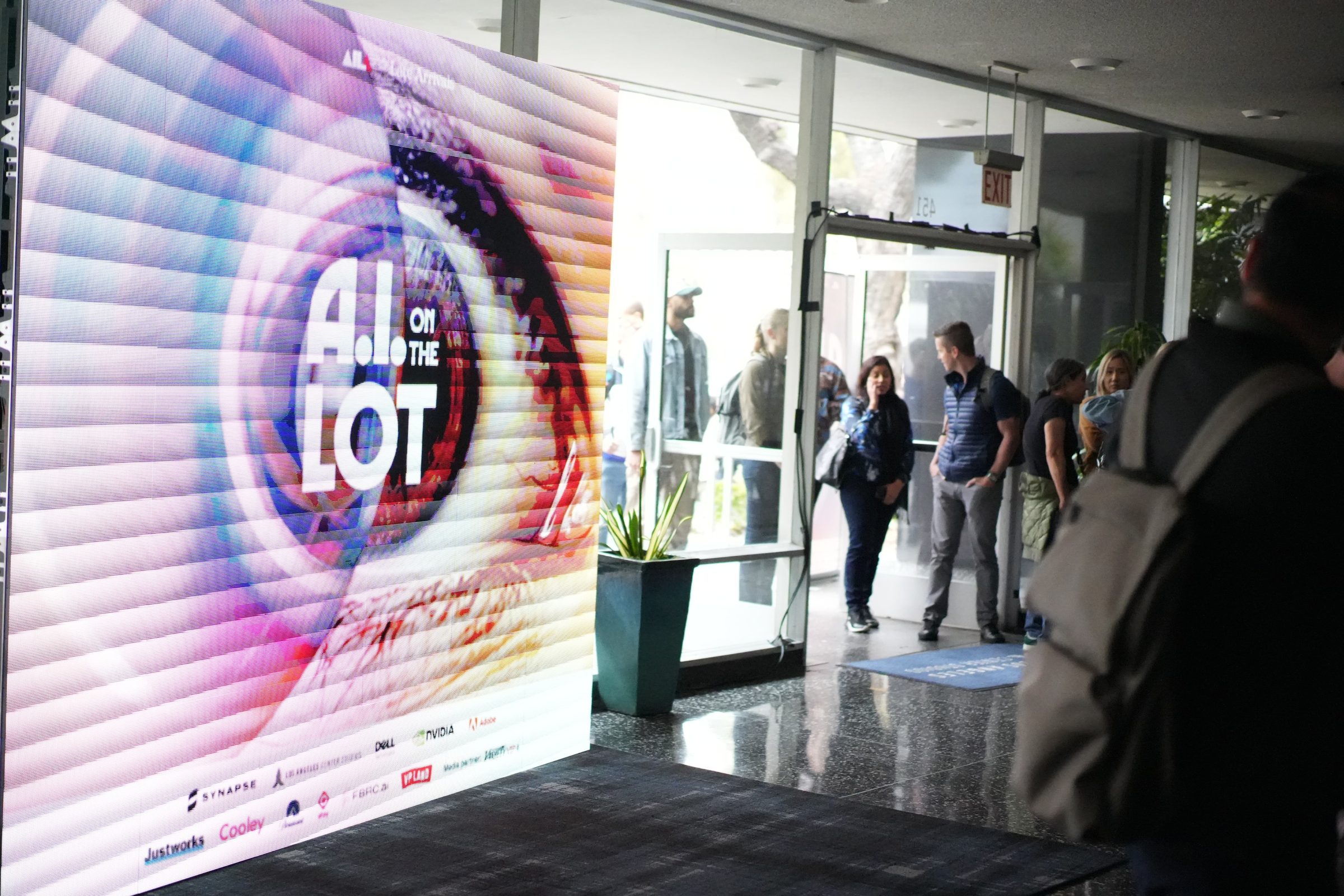 Attendees walk through glass doors past a large screen showing the AI on the Lot eye logo.