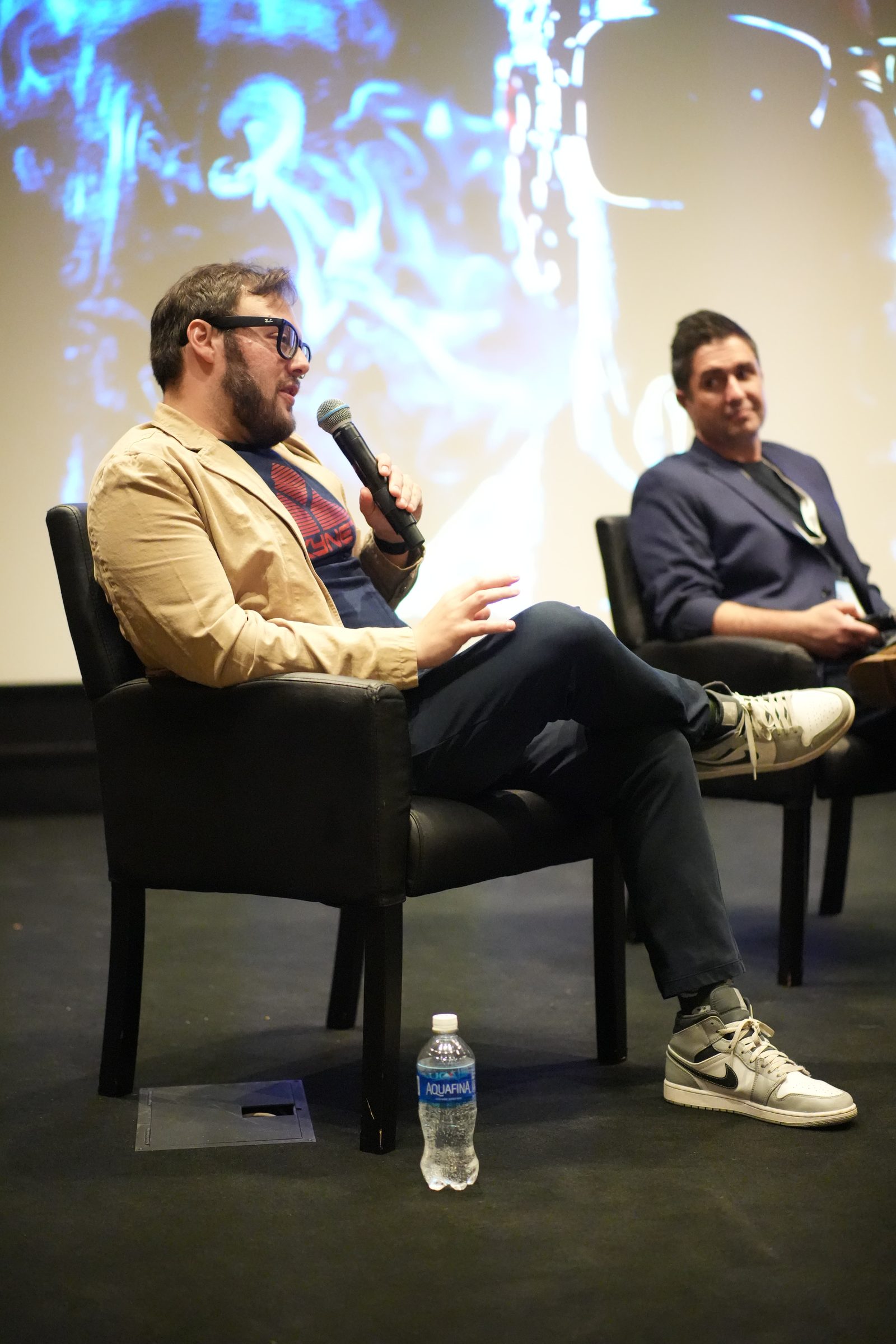 Max Einhorn speaks into a microphone from an armchair, a fellow panelist beside him.