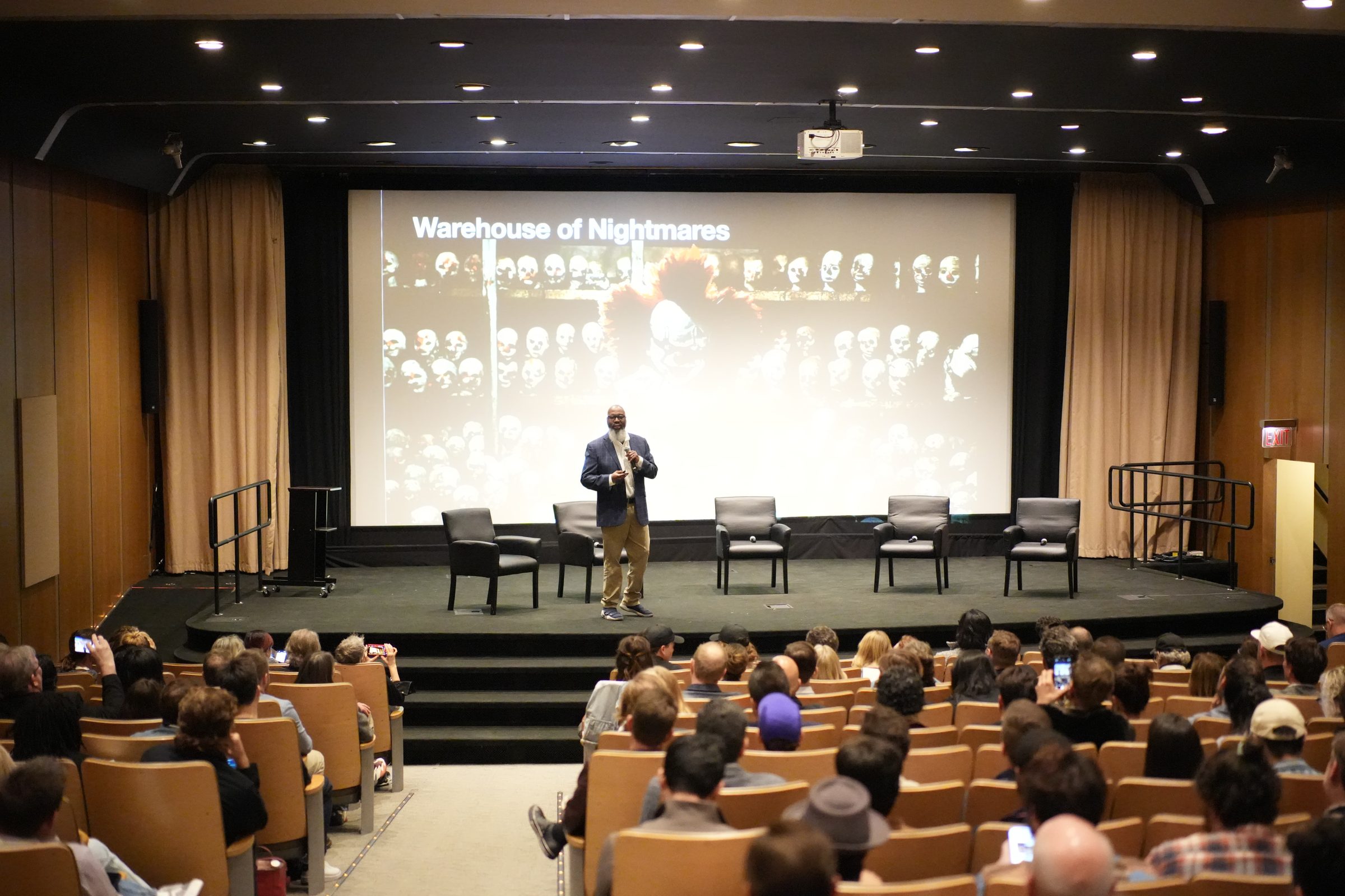 Renard Jenkins on stage before a full auditorium, the screen behind him reading Warehouse of Nightmares.