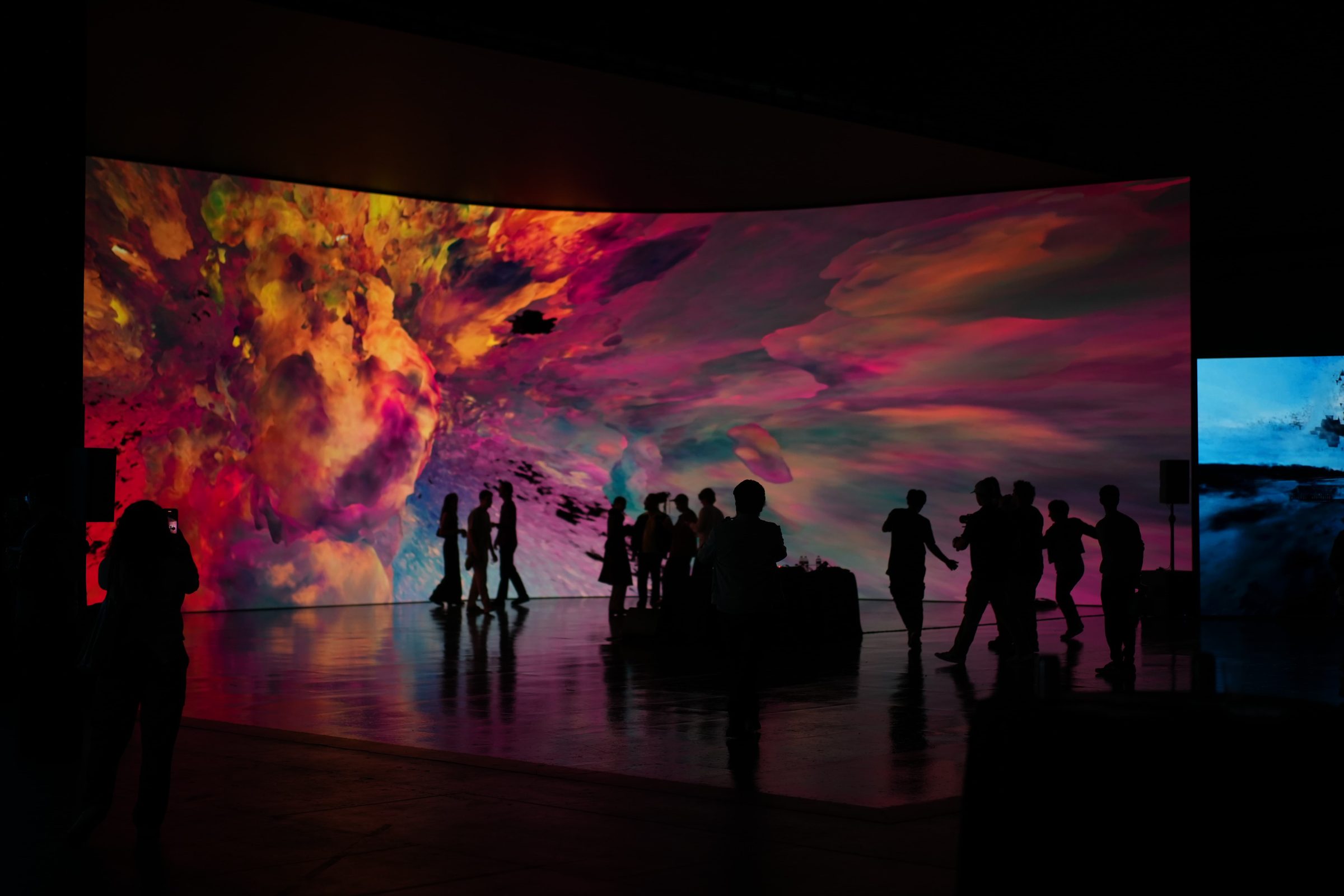 Silhouettes of attendees on a virtual production stage in front of a sweeping red and gold screen.