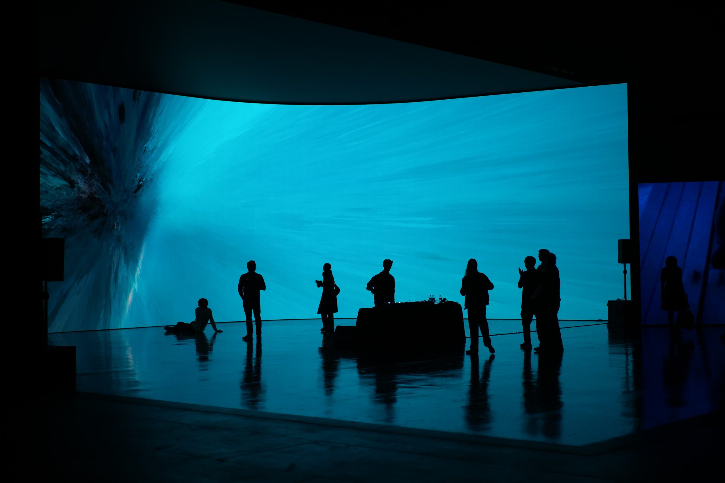 People stand as silhouettes against a curved blue virtual production screen.