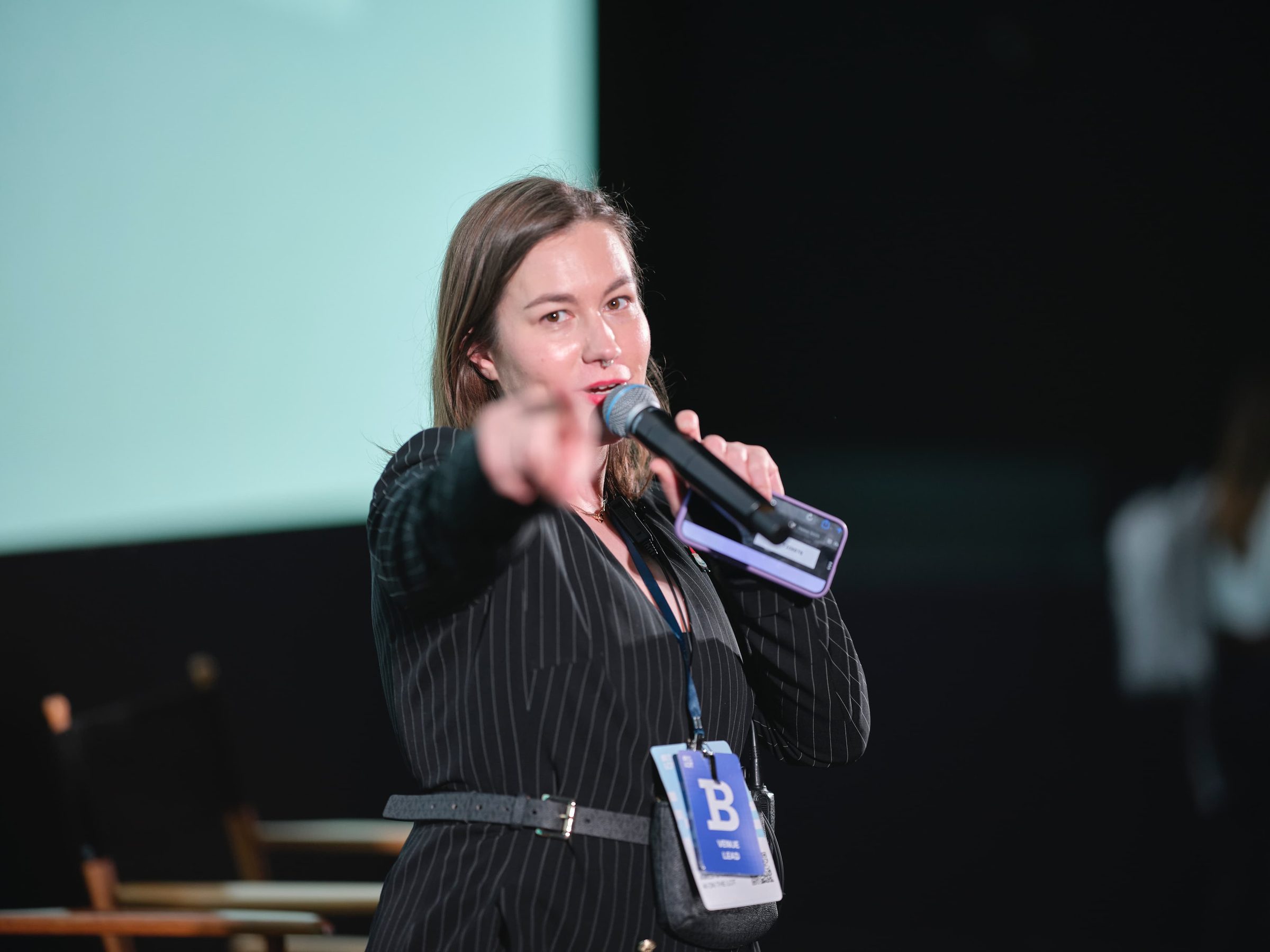 Ames O'Connor, in a pinstripe suit, points toward the crowd while speaking into a microphone.