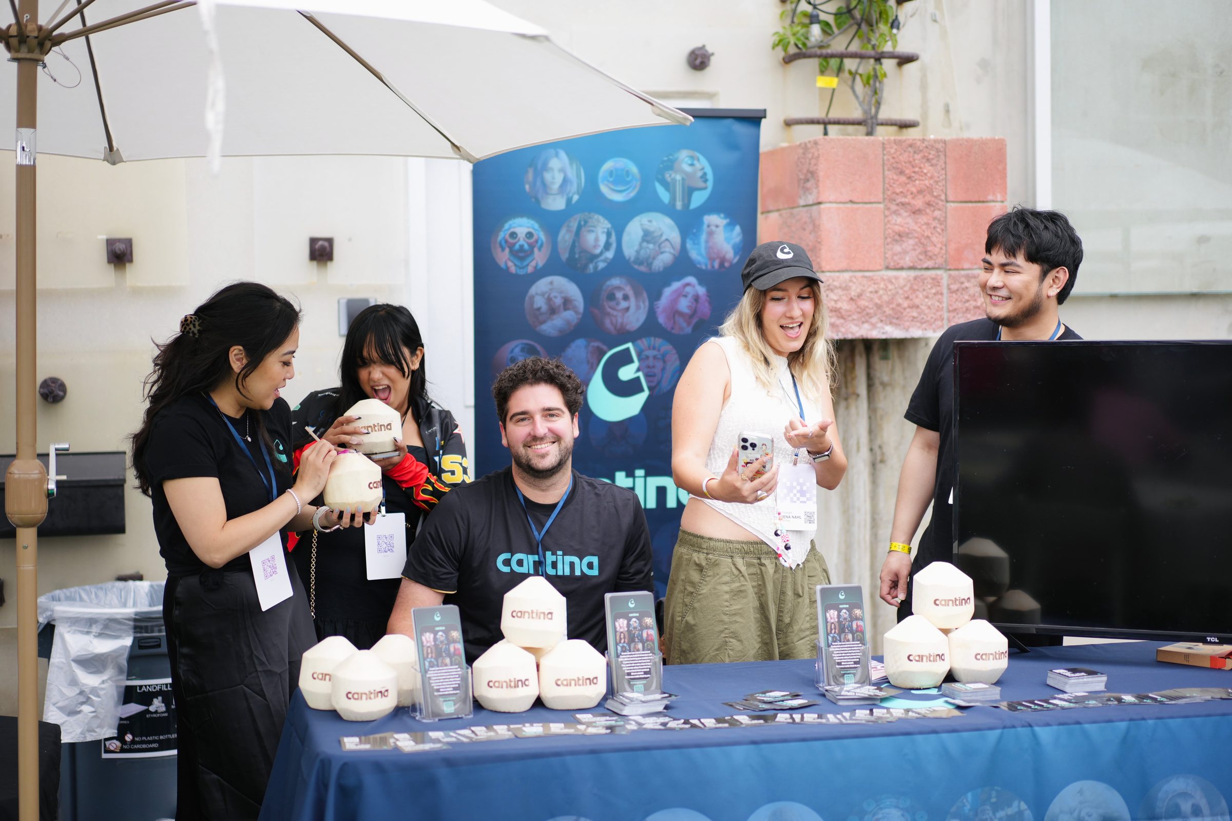 Cantina AI staff smile behind a table stacked with coconuts, a character banner behind them.