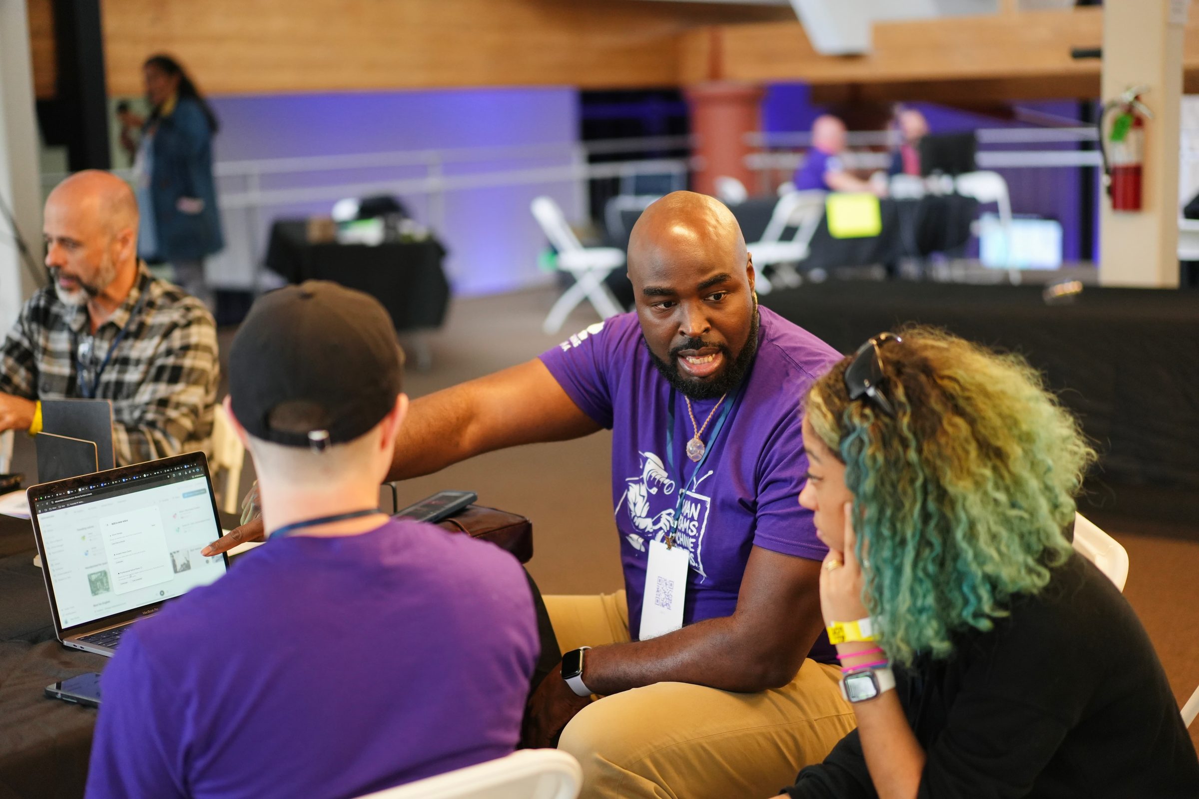 A docent in a purple shirt leans in to walk two attendees through a laptop.