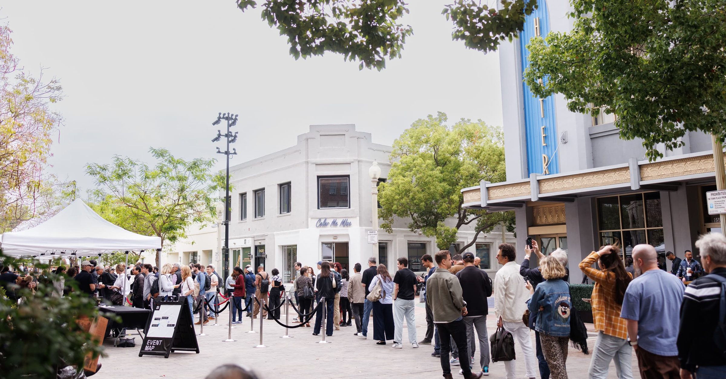 A long line of attendees waits outside the white Culver Theater under a clear sky.