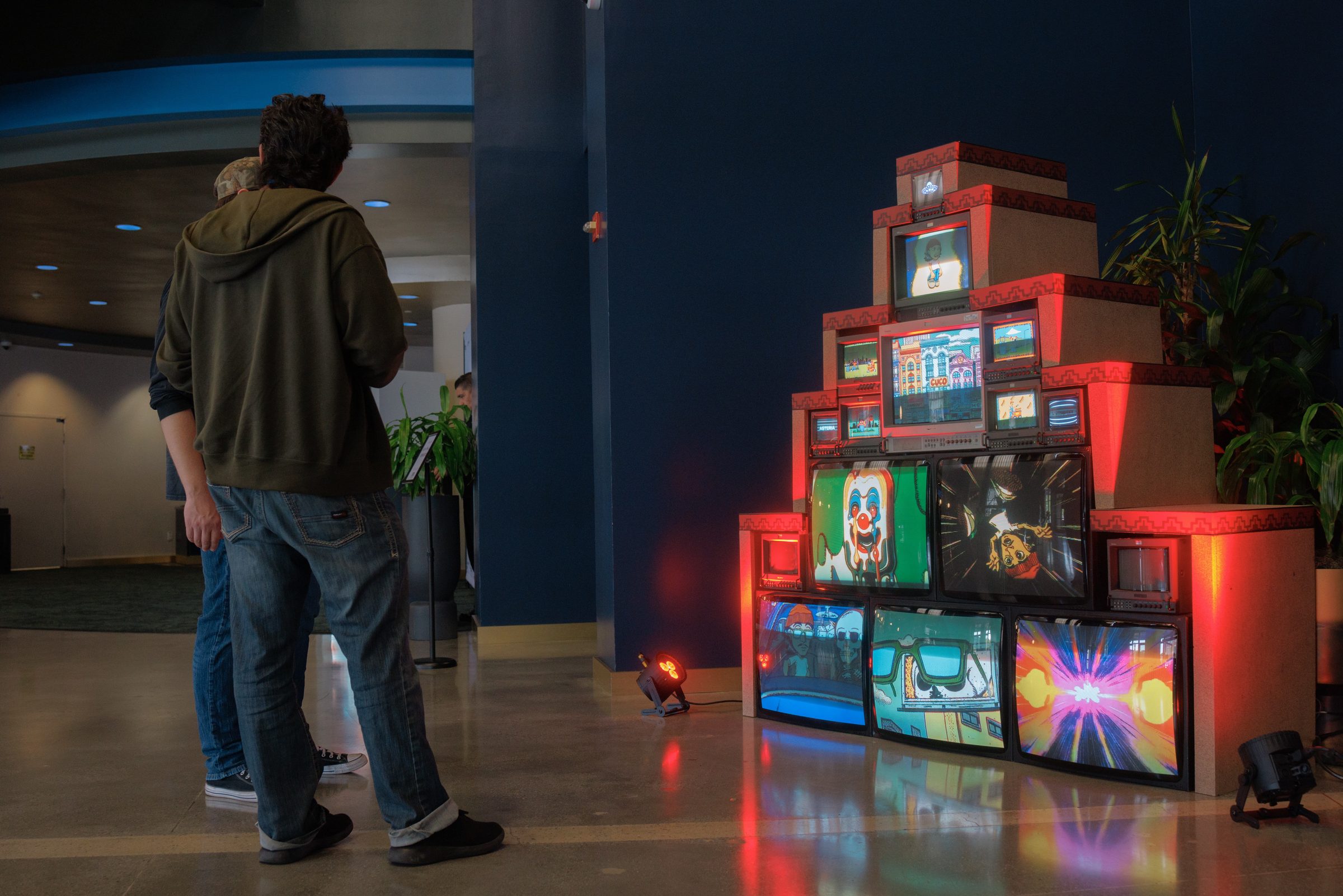 A stack of glowing CRT televisions and red boxes, an attendee standing in front of it.