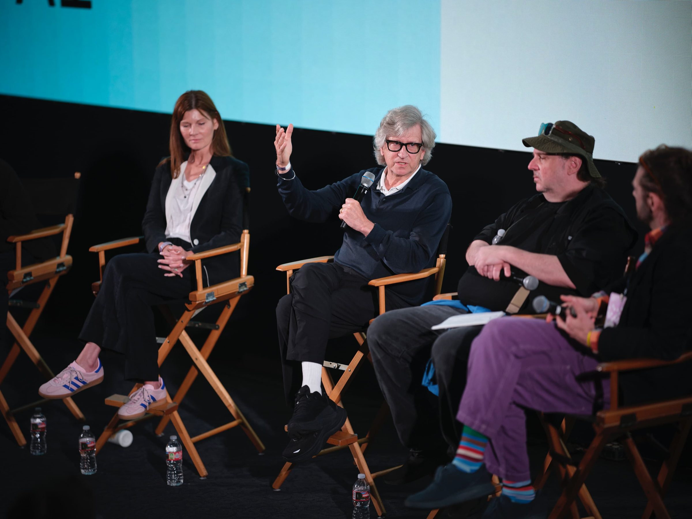 Rick Carter gestures from a director's chair during a panel, three panelists seated beside him.
