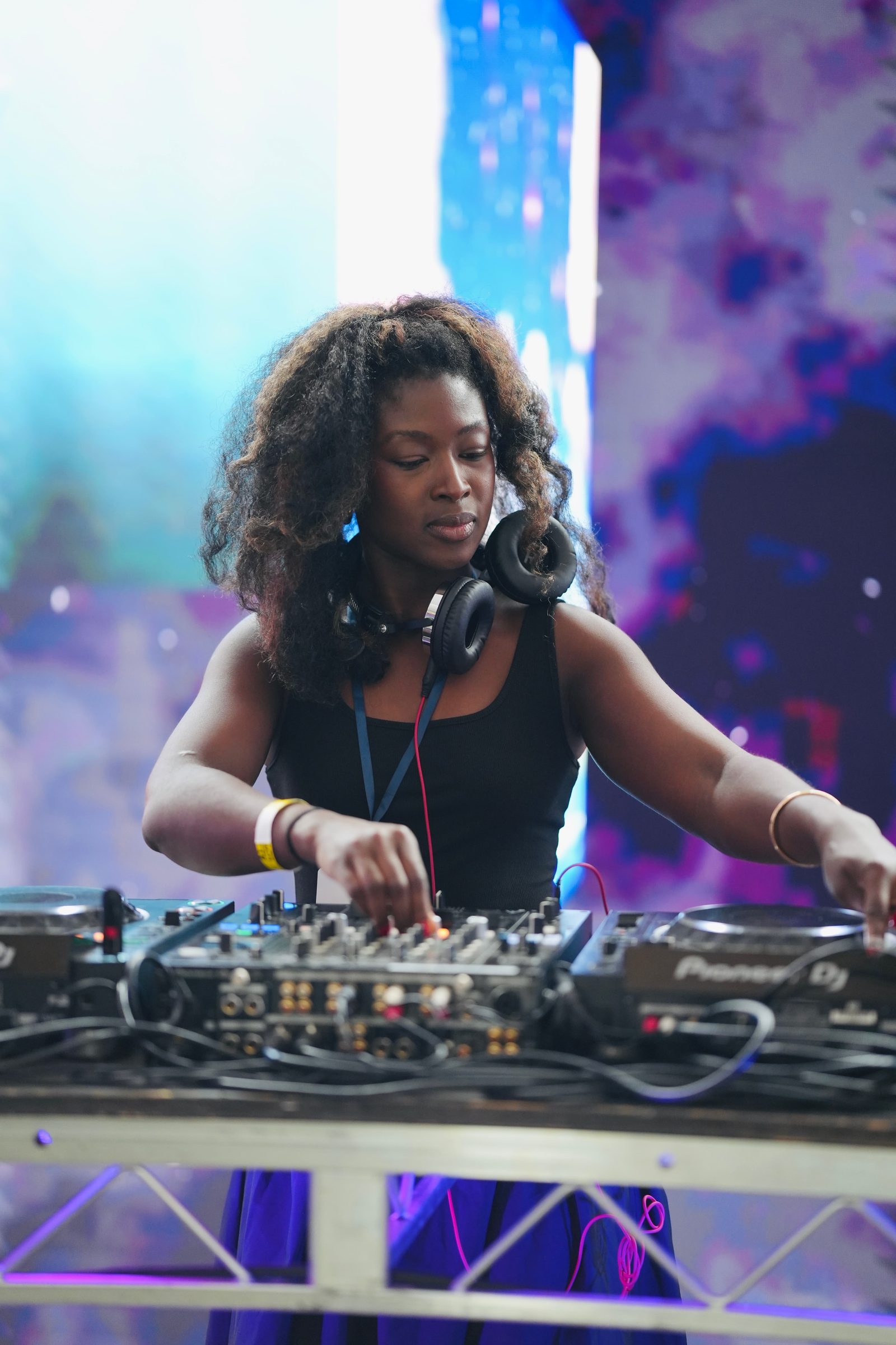 Val Fleury, headphones on, mixes a set behind a DJ deck in pink and blue light.