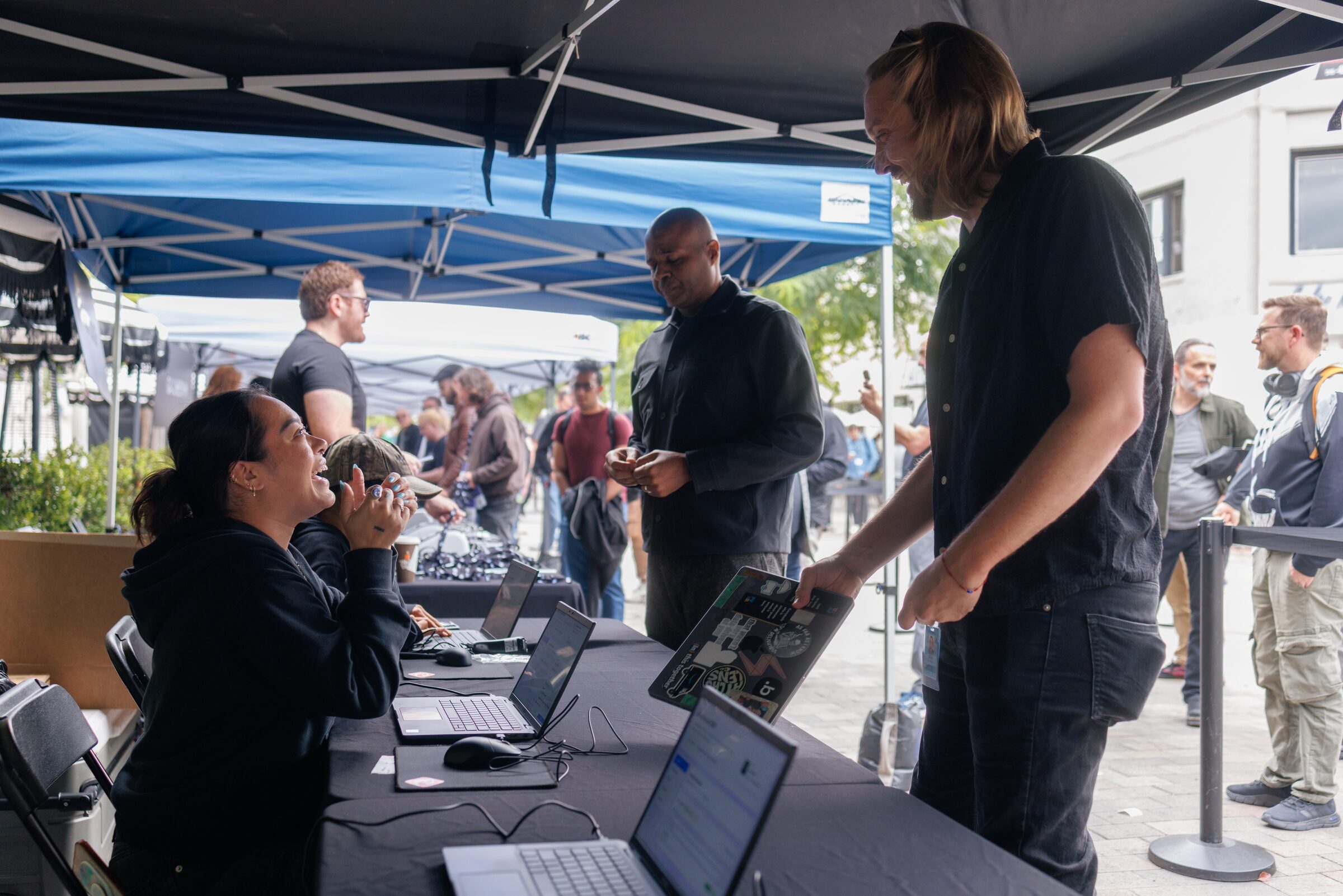 An attendee holds out his phone at a laptop-lined registration table as volunteers check in the line.