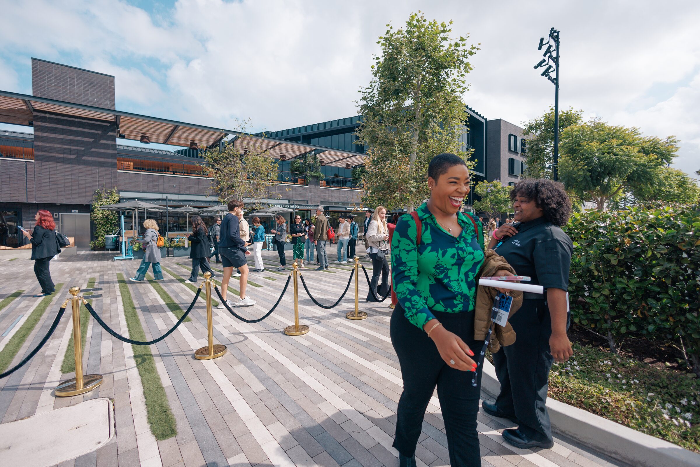 A smiling attendee in a green floral blouse walks along a roped-off path on the lot beside a friend.