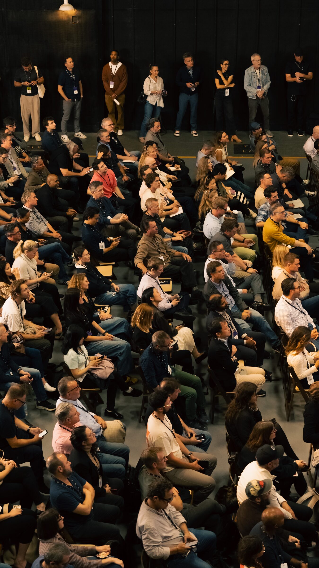 Seen from above, a seated crowd fills every chair while more attendees stand along the back wall.