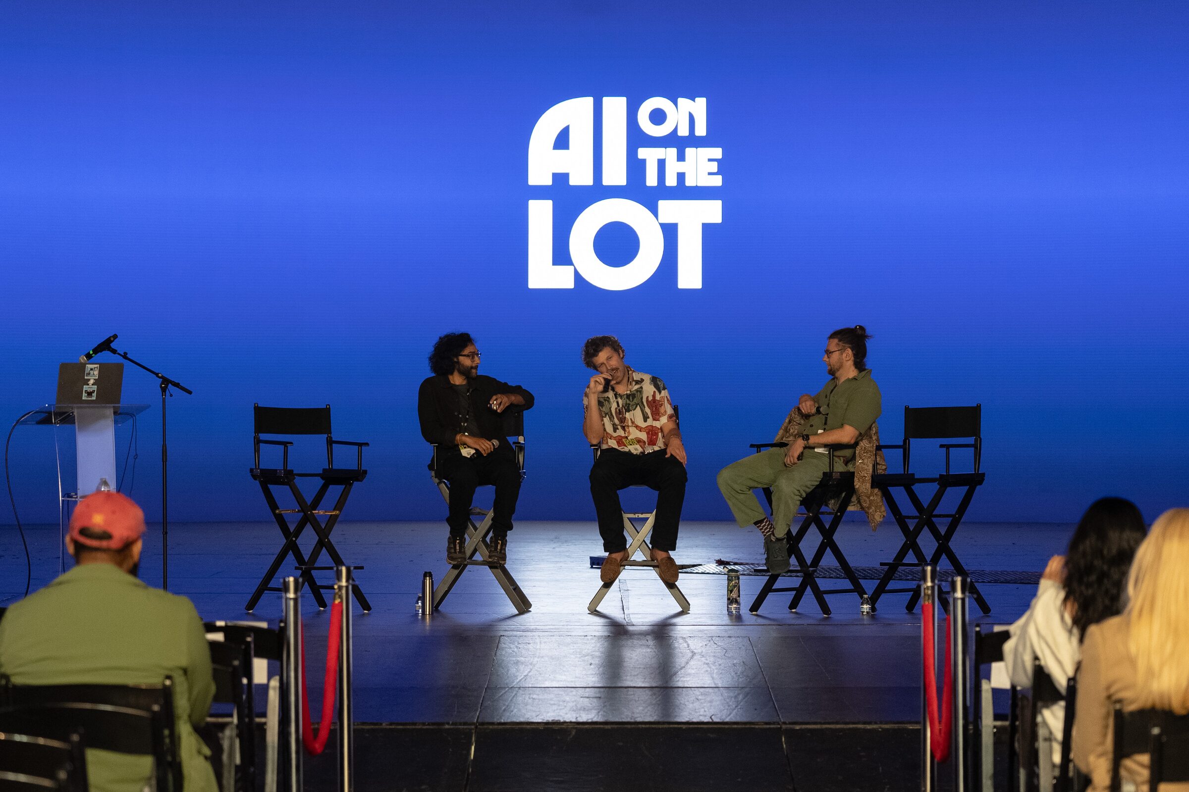 Ian Eck and two fellow speakers in director's chairs on the blue stage, the AI on the Lot logo above, crowd in front.