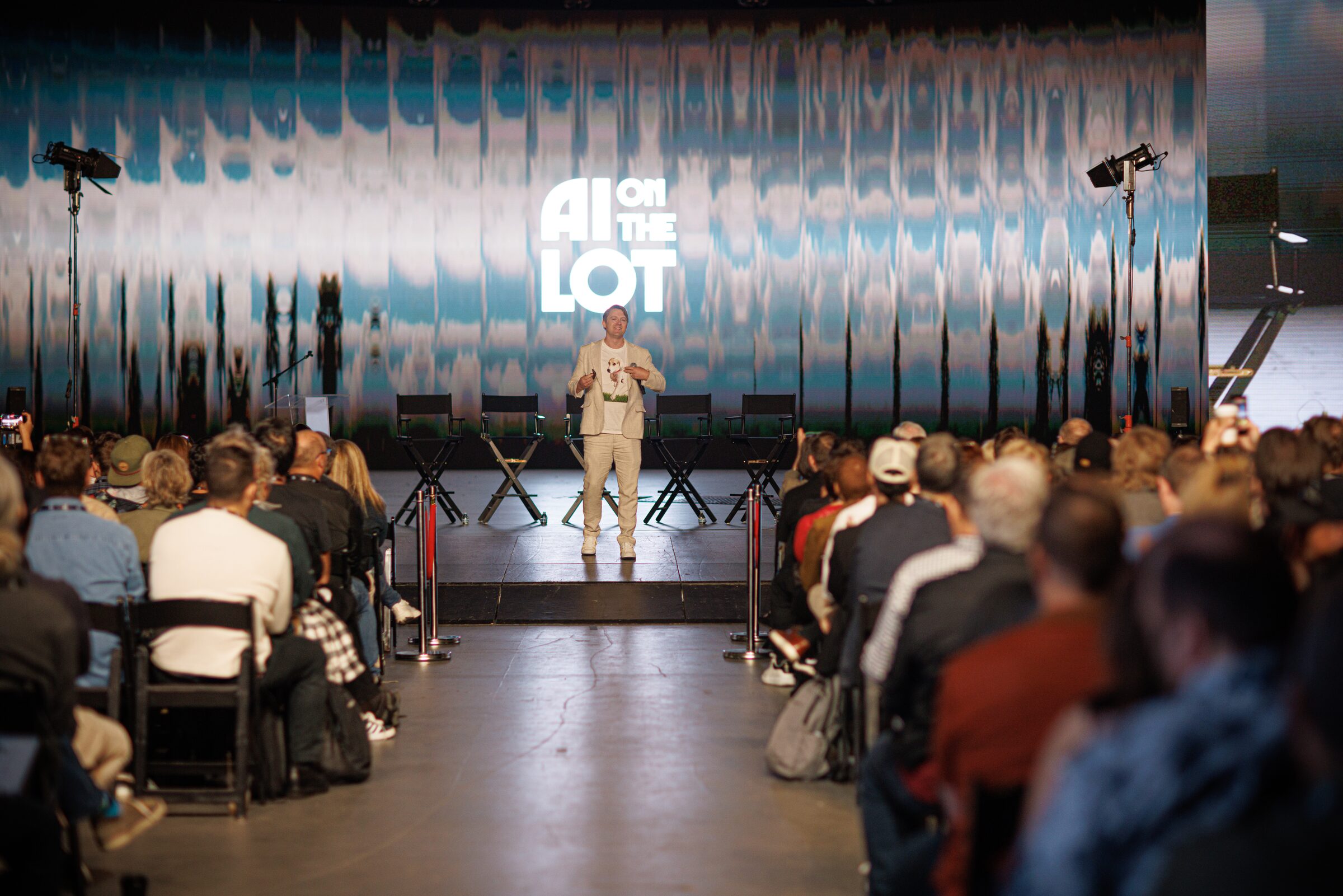 Todd Terrazas in a cream suit stands center stage under the AI on the Lot logo, a full audience on both sides.