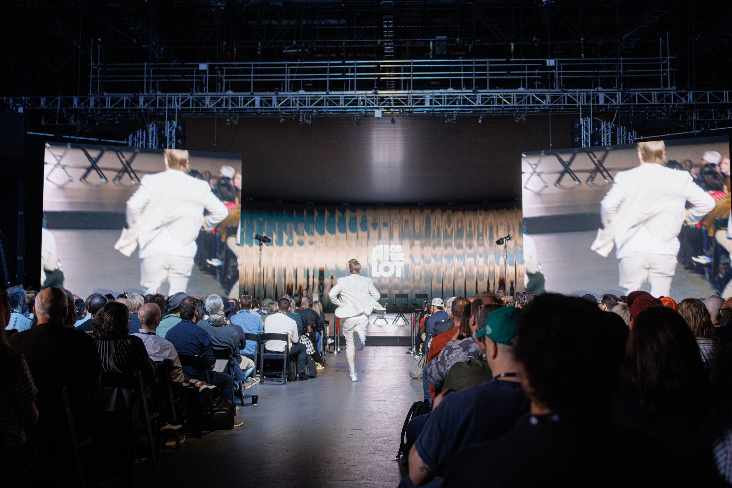 Todd Terrazas, in a white suit, runs down the center aisle to the stage, shown on big screens on both sides.