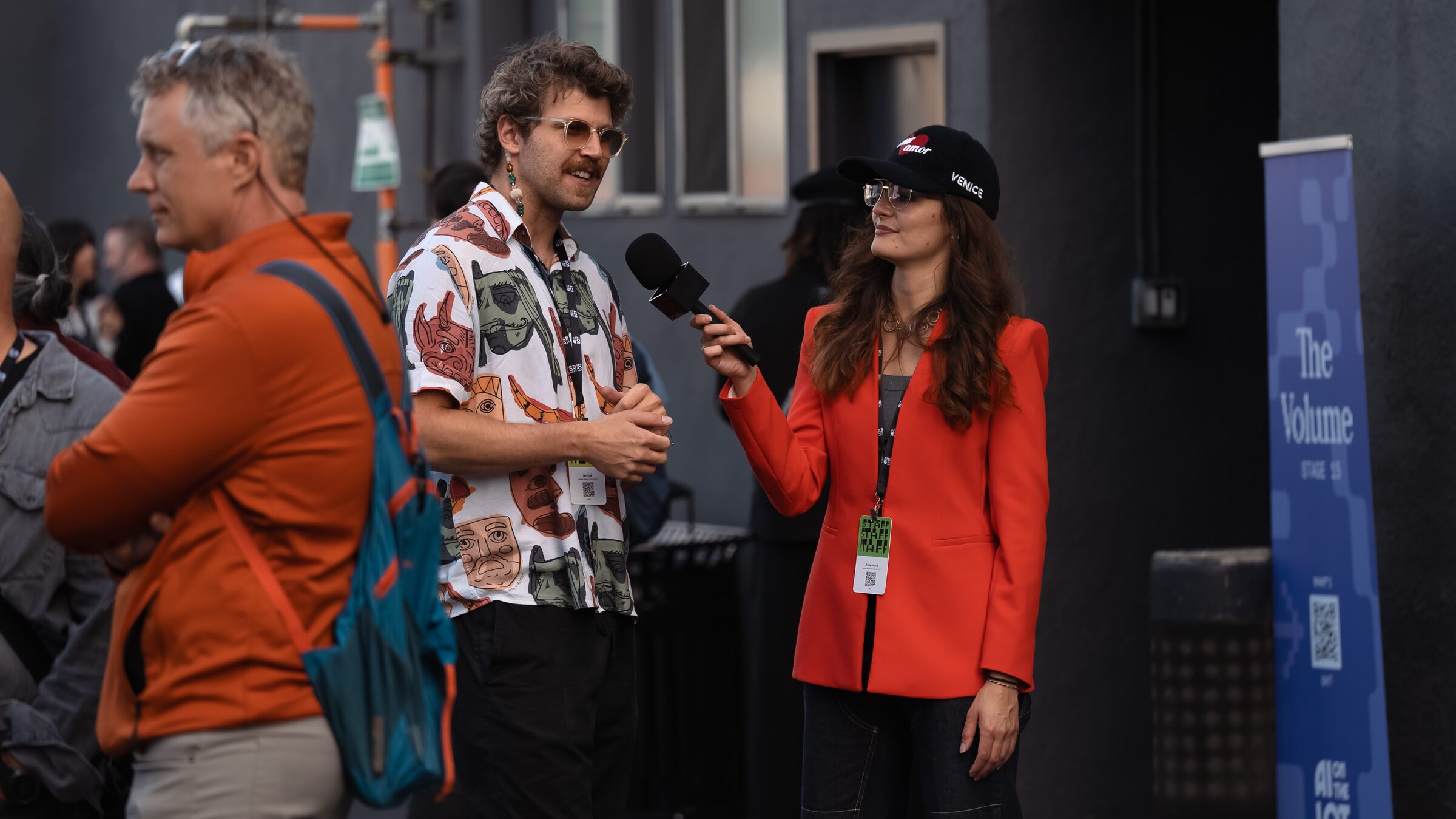 Ian Eck answers reporter Julia Harris's questions into her handheld mic, a man in an orange jacket beside them.