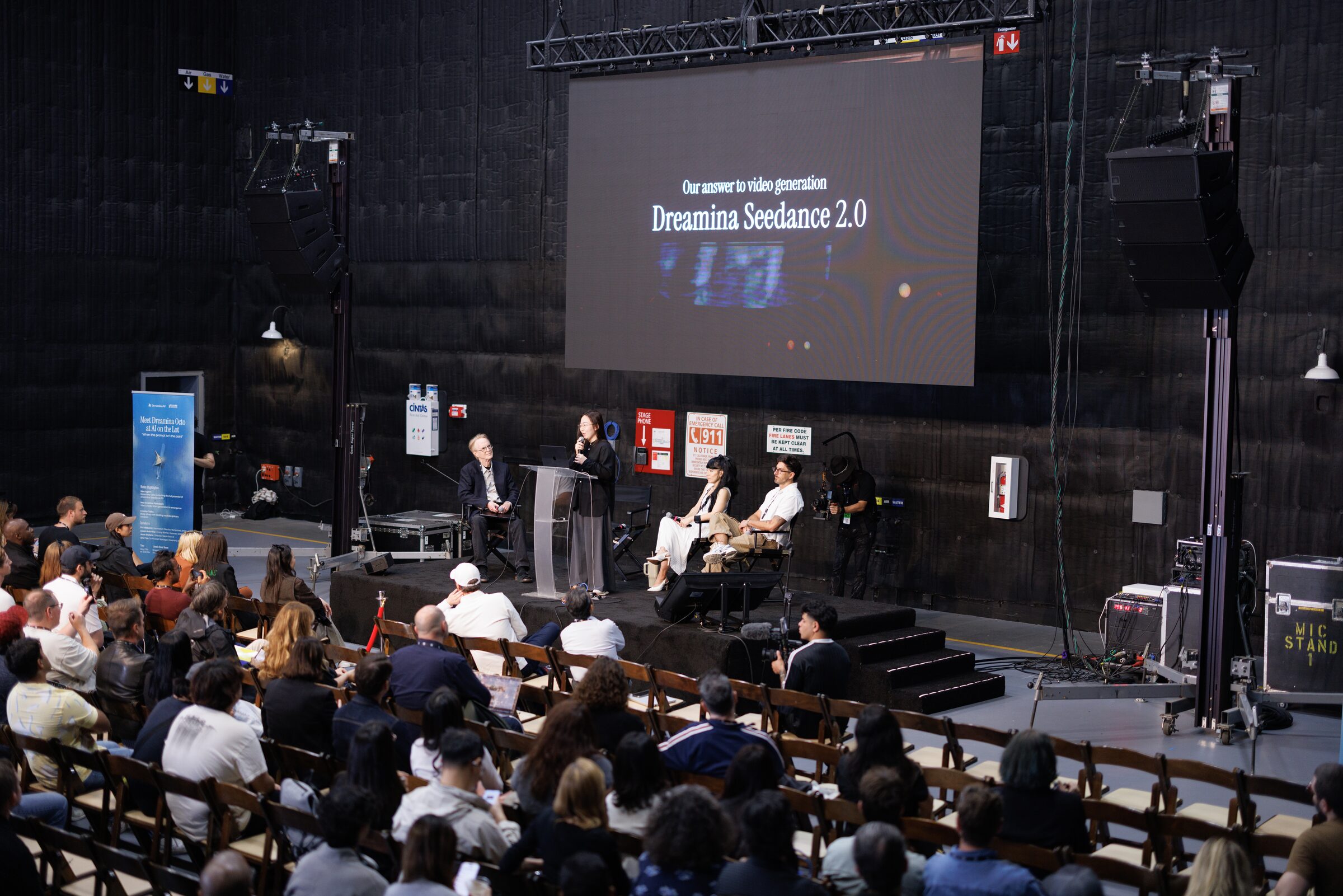 Speakers on a small stage under a big screen reading "Dreamina Seedance 2.0," facing a full audience.