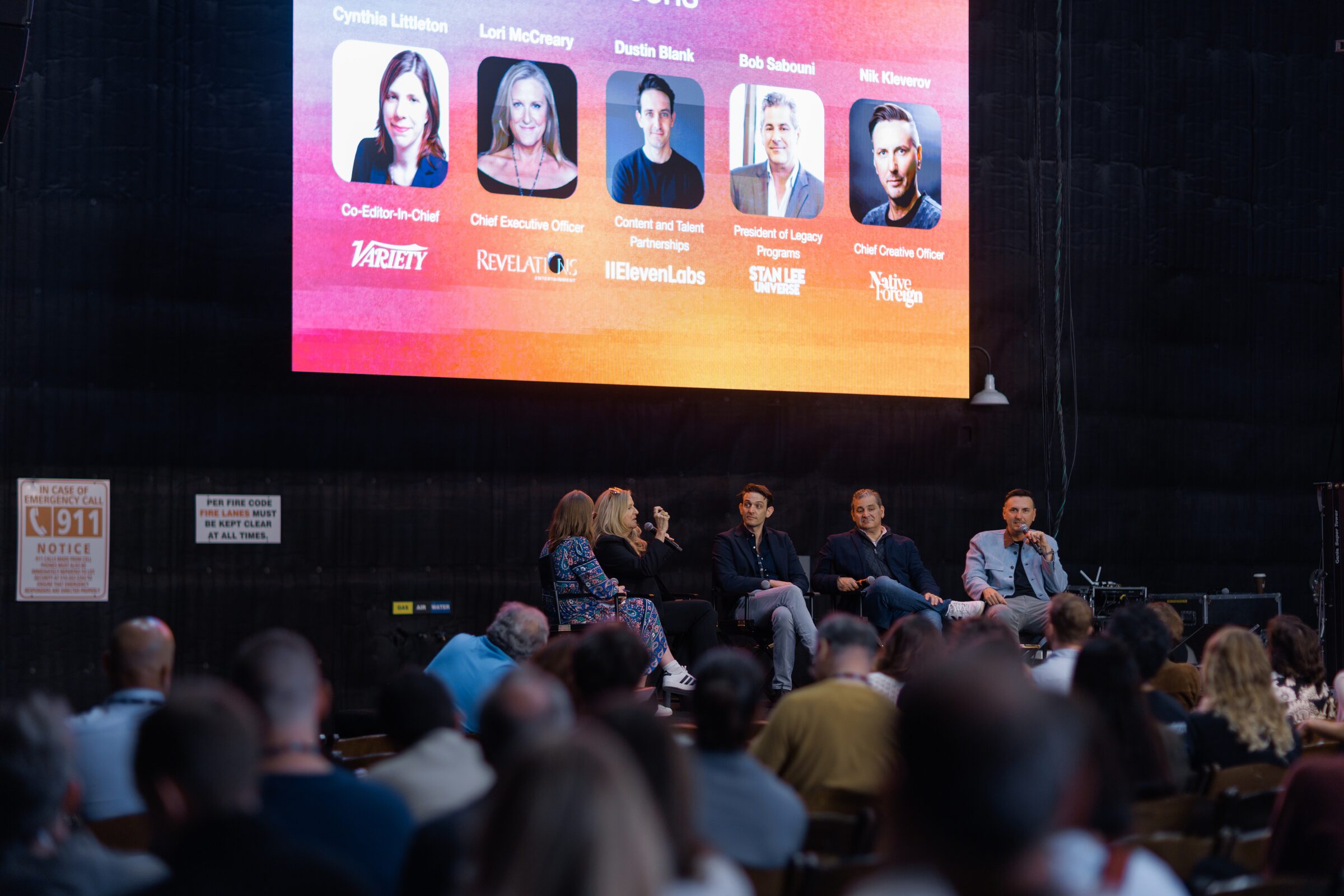 Five panelists sit before a big screen showing their headshots and logos, including ElevenLabs and Stan Lee's.