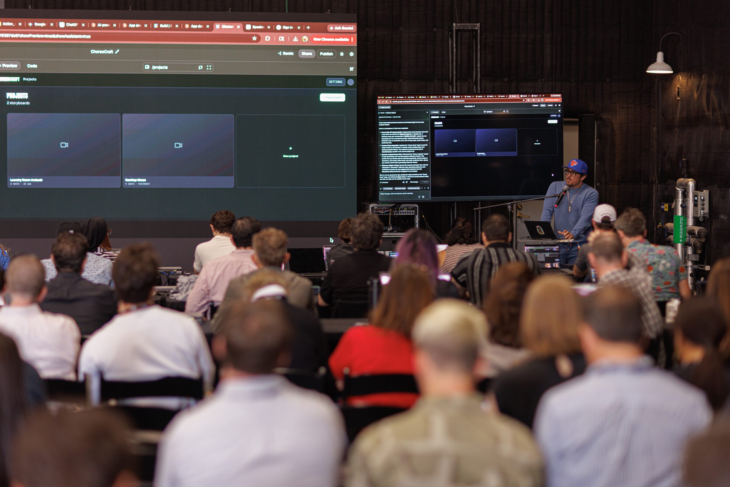 Squid speaks at a mic beside two big screens of code and video tools, a packed workshop facing him.