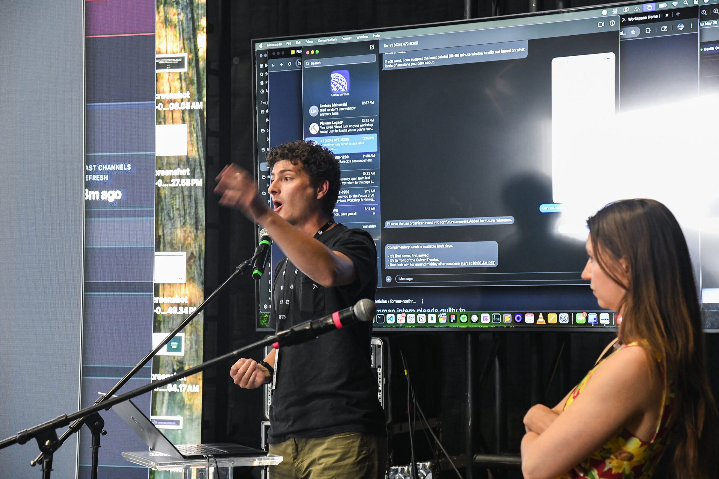 Nathaniel Mahowald points to a big screen as he speaks at a mic, an attendee in a floral dress listening nearby.