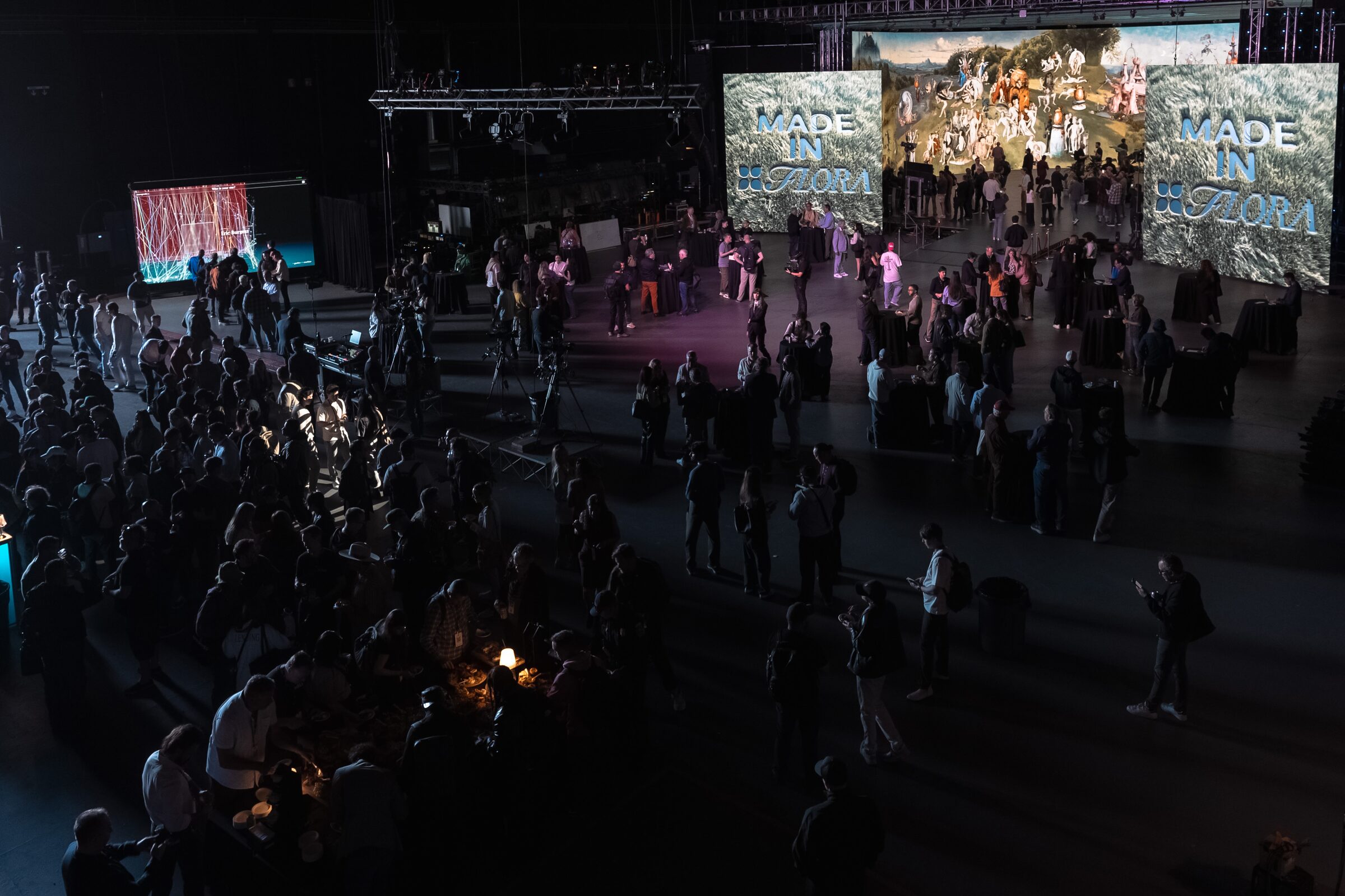 Seen from above, a happy hour crowd mills around giant "Made in Ozora" screens of surreal painted art.