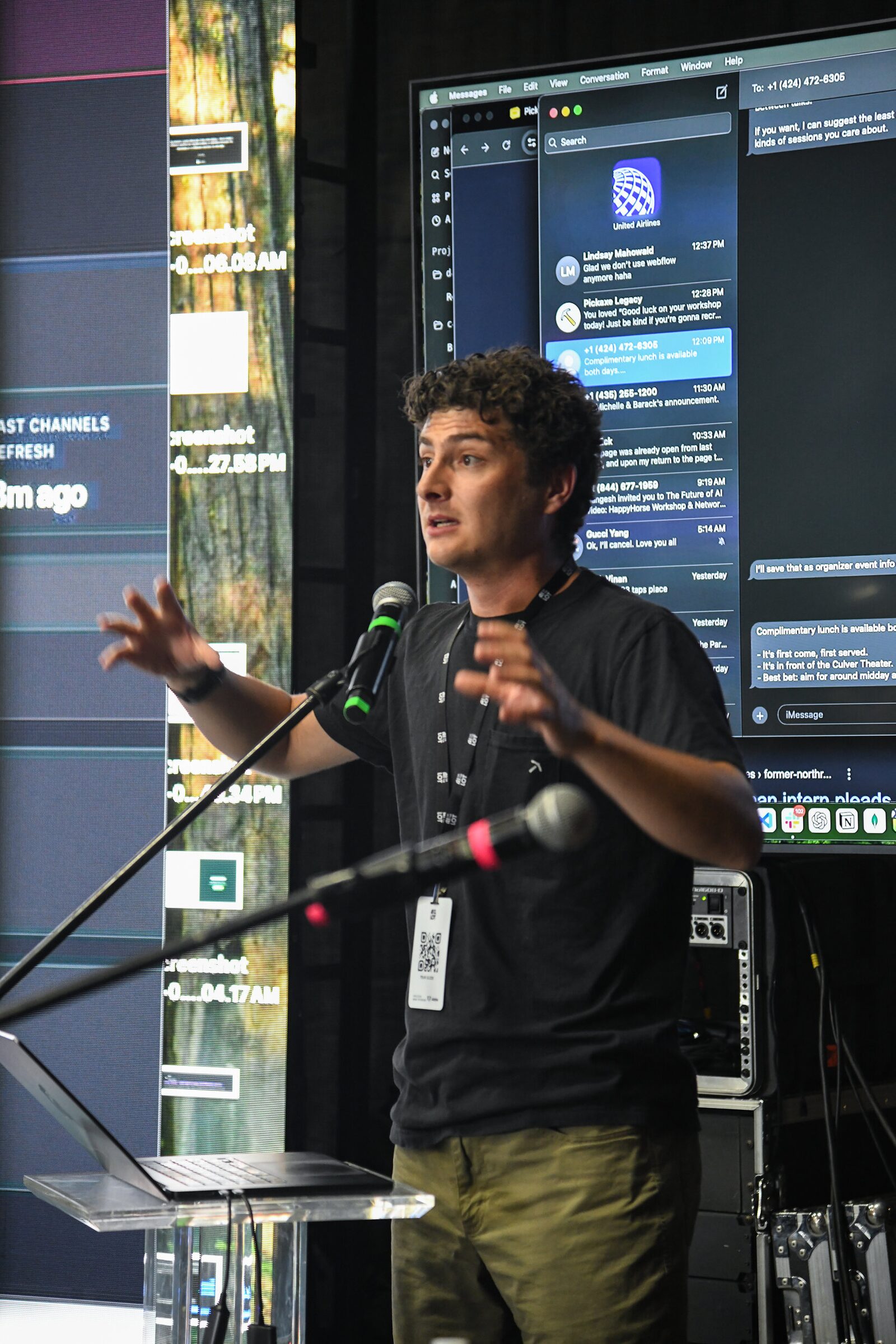 Nathaniel Mahowald gestures at a mic in a black T-shirt, a big screen of chat messages glowing behind him.