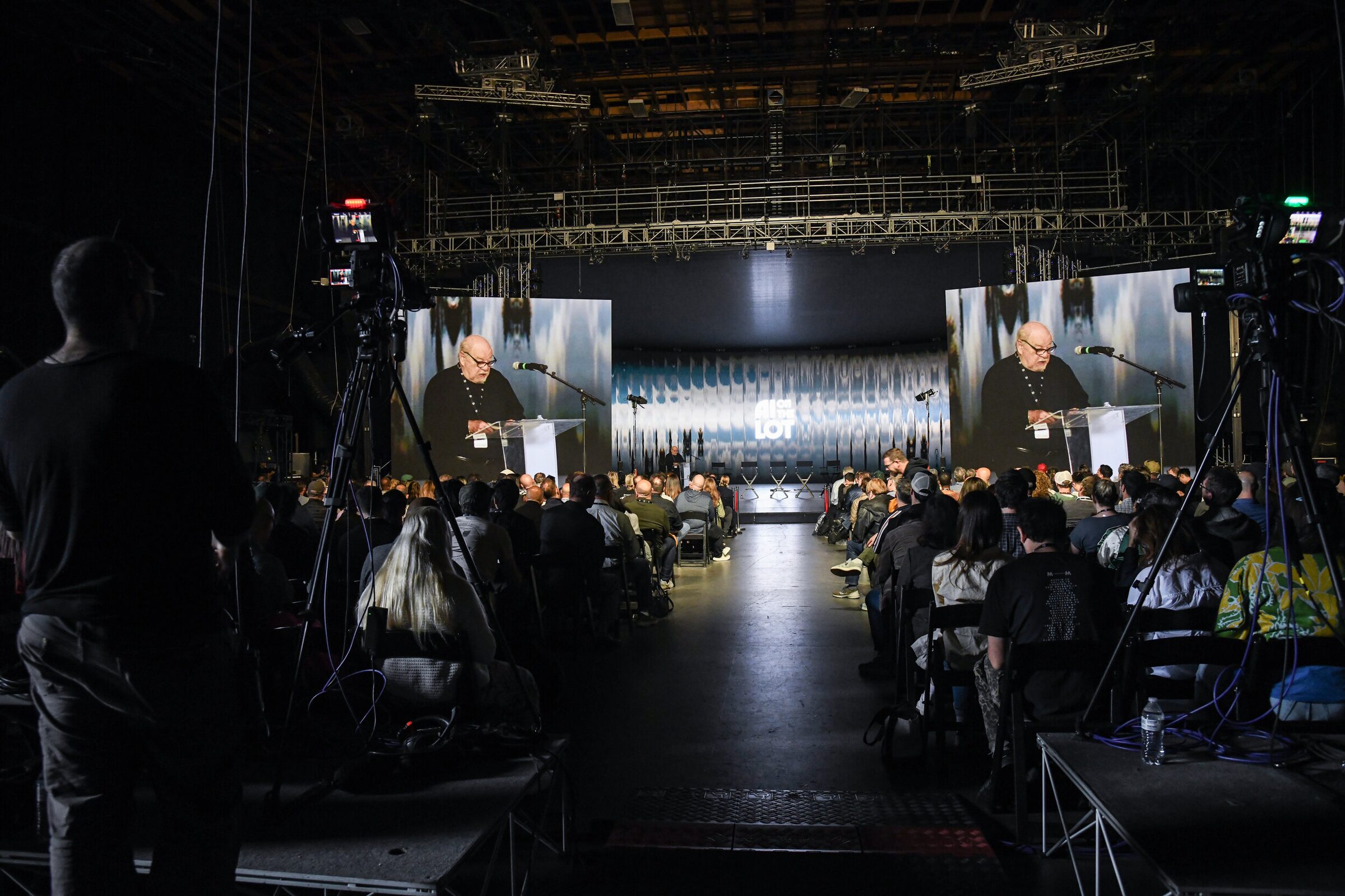 The center aisle of a full Stage 15 between camera rigs, Paul Schrader on the stage and on twin screens.