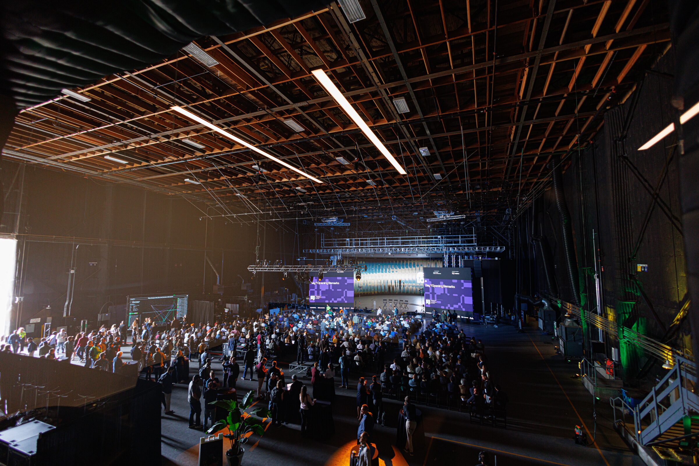 From high above, a sea of seated attendees fills the vast Stage 15 under its lighting grid, screens glowing.