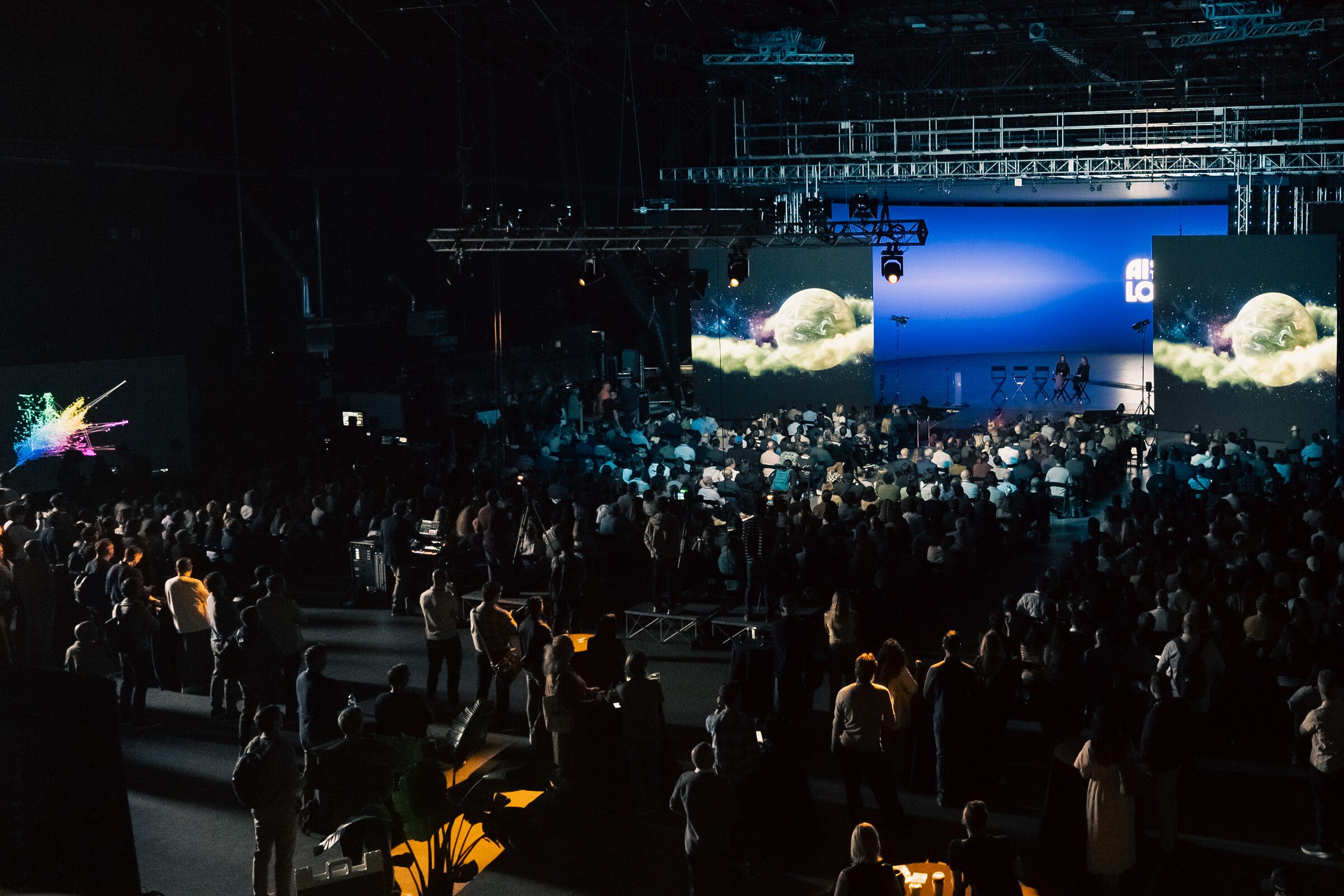 A huge, dark Stage 15 crowd faces the far stage, its twin screens showing a glowing AI-made fantasy world.