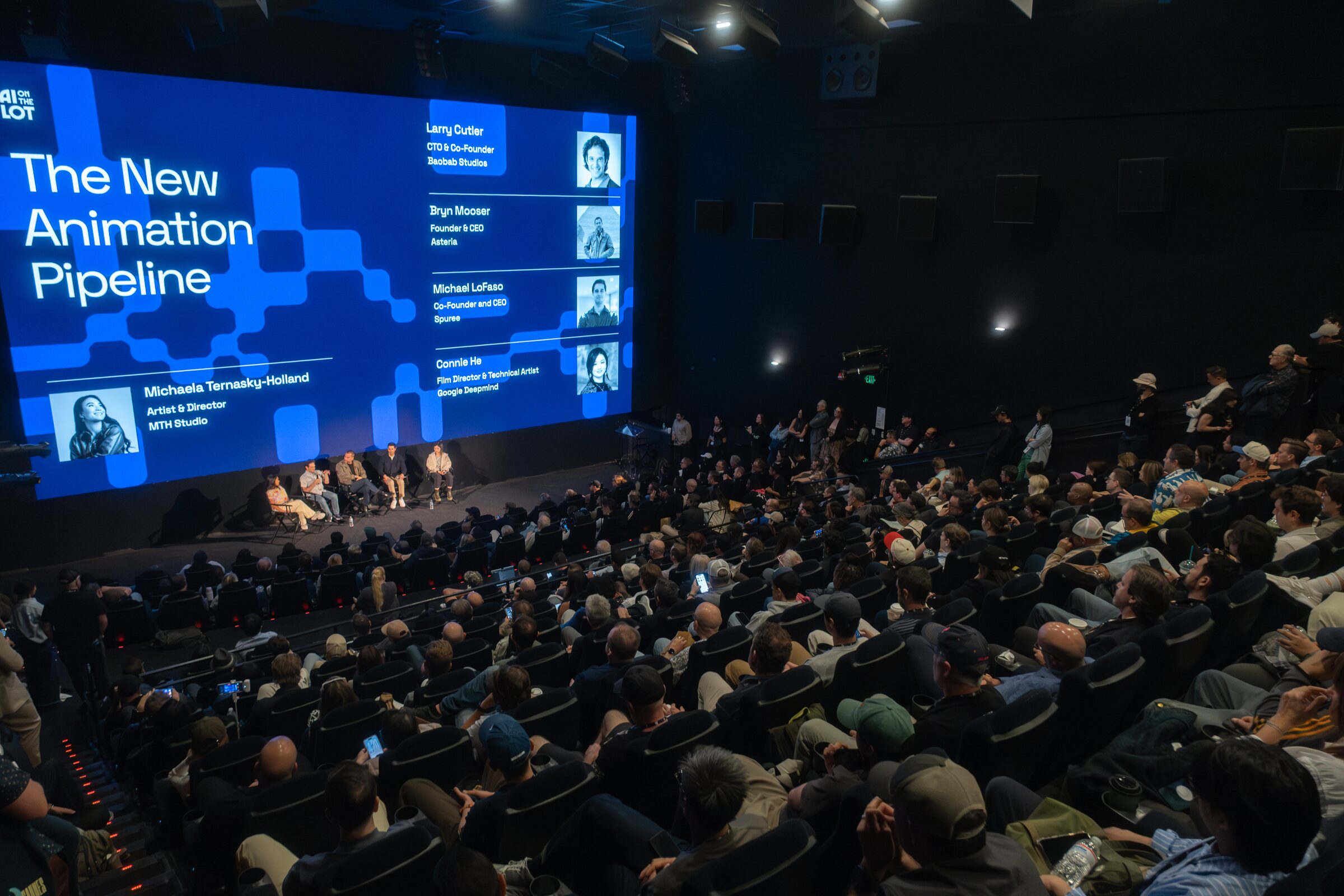 A full, raked theater watches a panel beneath a giant screen reading "The New Animation Pipeline."