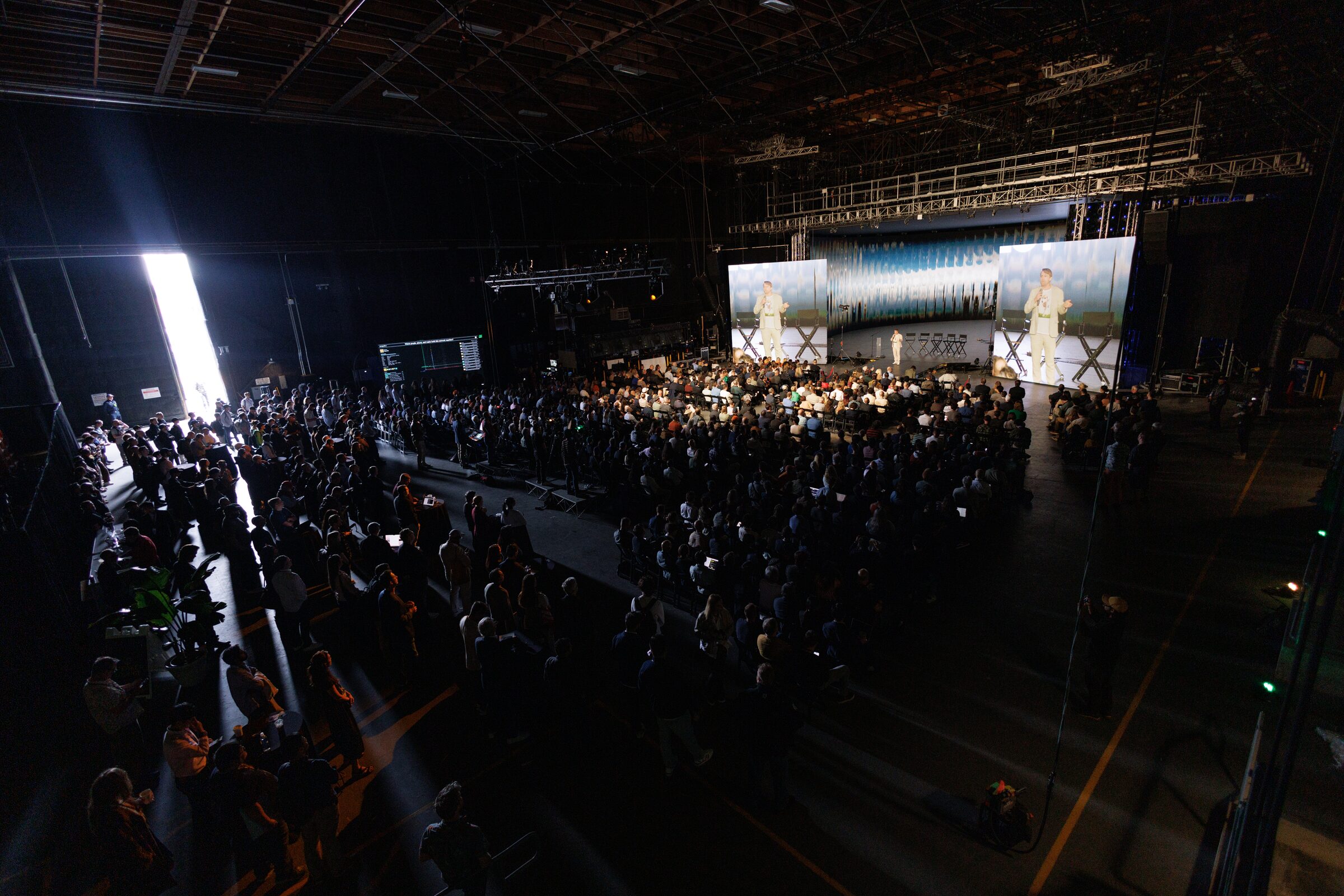 Todd Terrazas on a distant stage and on twin screens, facing a vast, dark crowd that fills Stage 15.