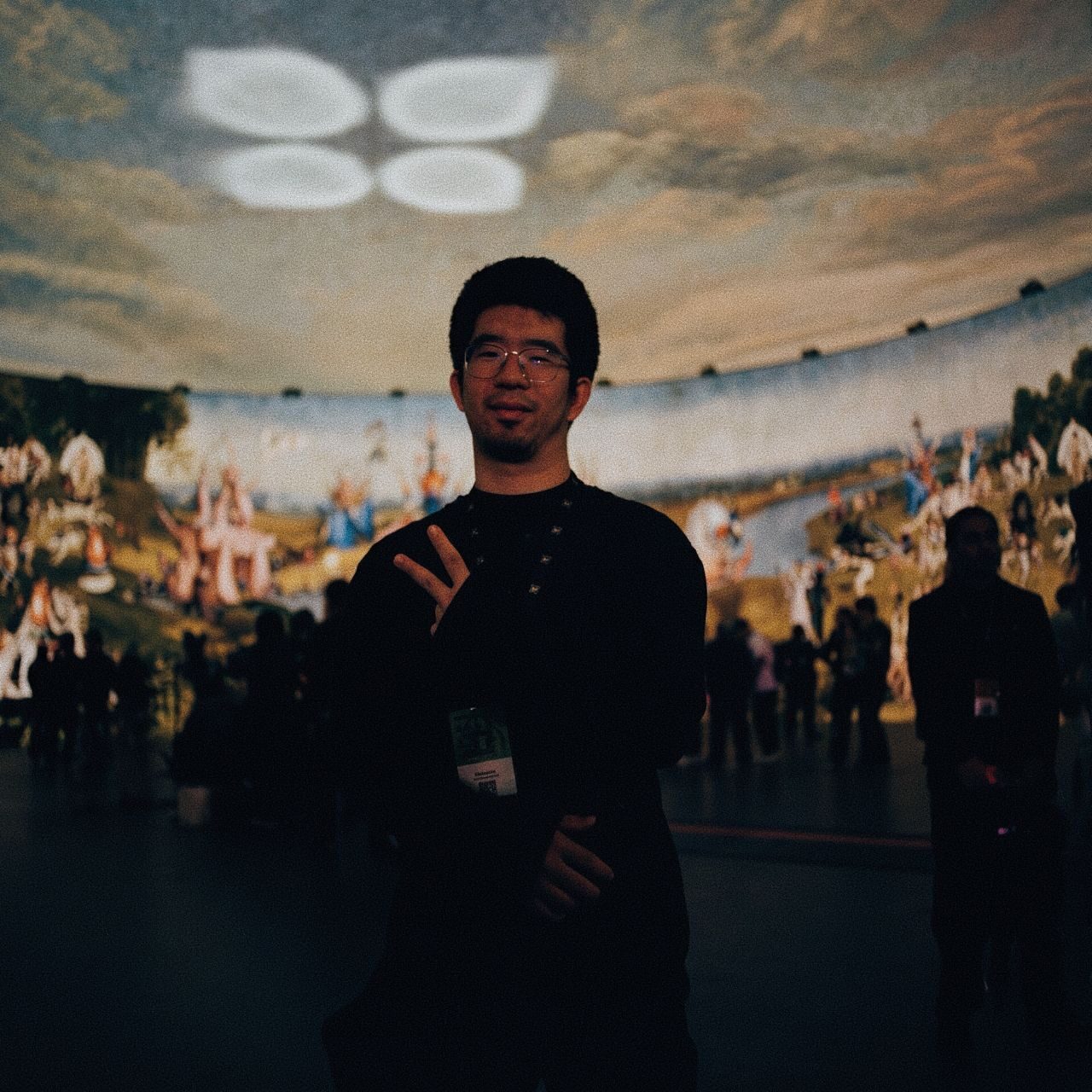 Tommy Wu, in glasses and black, stands inside a dome of projected Hieronymus Bosch paintings, visitors behind him.