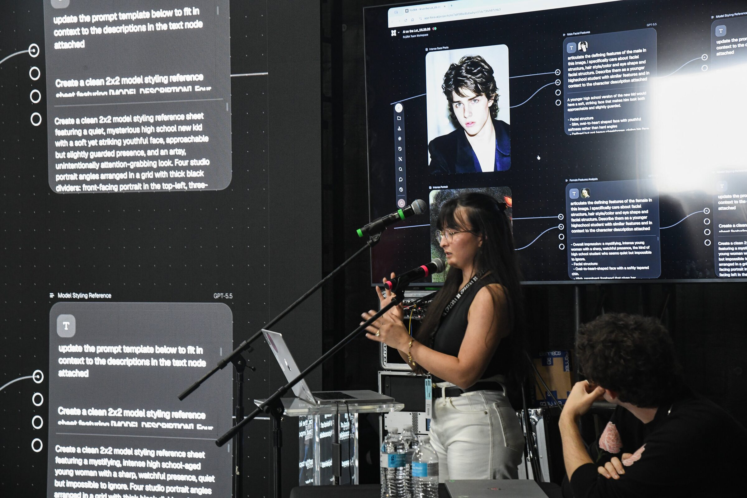 A presenter at a mic beside a giant screen of a node-based AI workflow building a character model sheet.